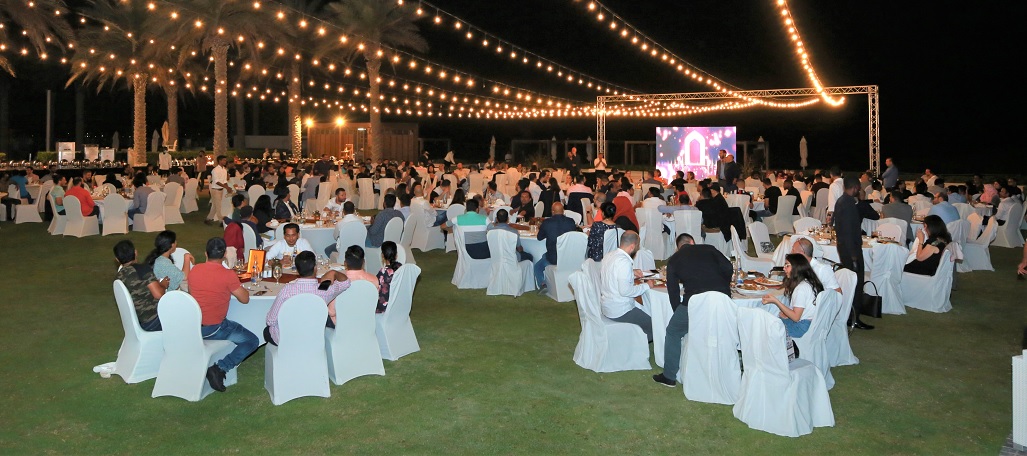an event with many tables of diners sitting under strings of decorative lights