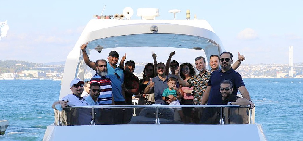 a group of people smile and wave across the rear of a boat to the camera