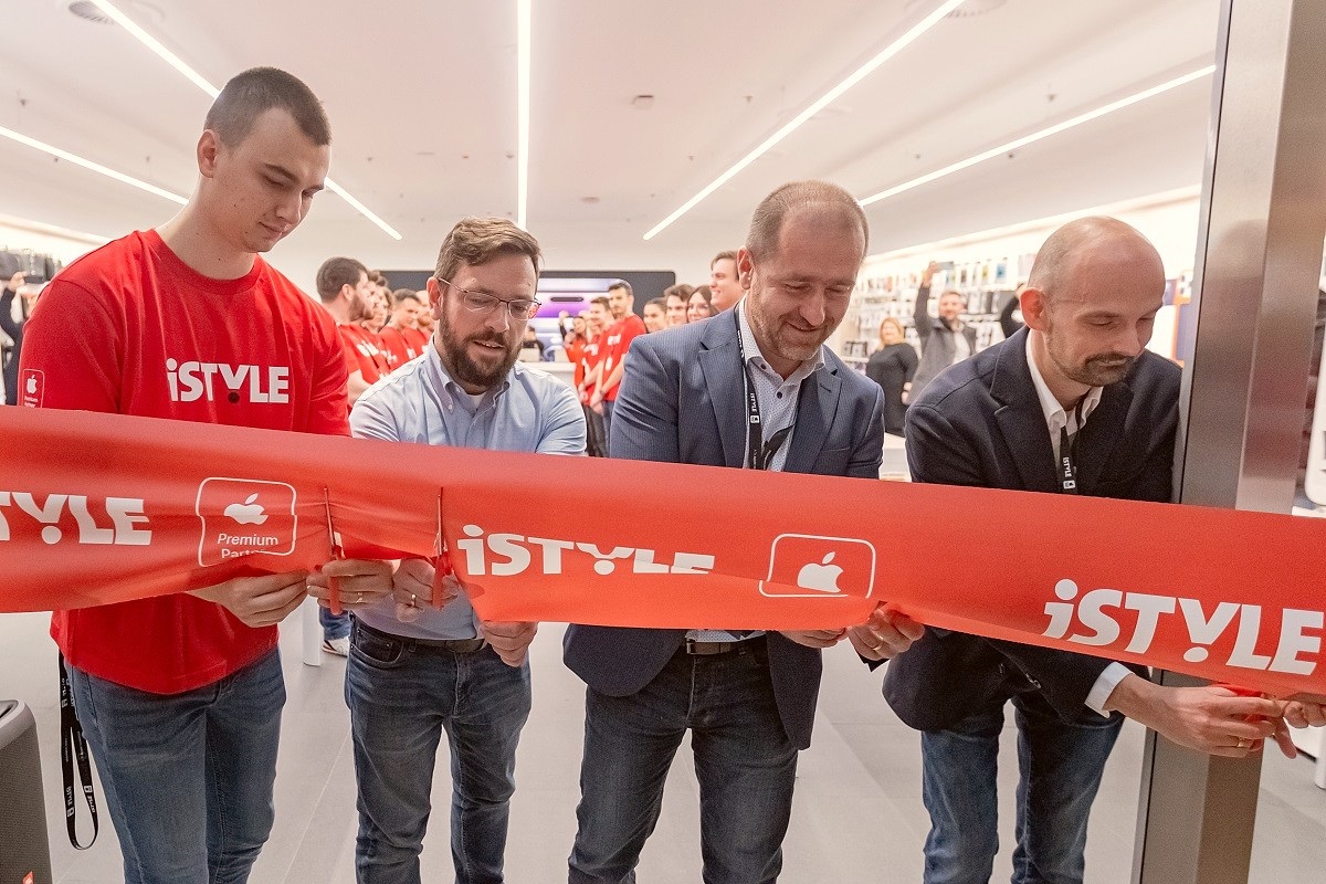 four men are seen cutting a big red ribbon stretched across the front of a hi tech store