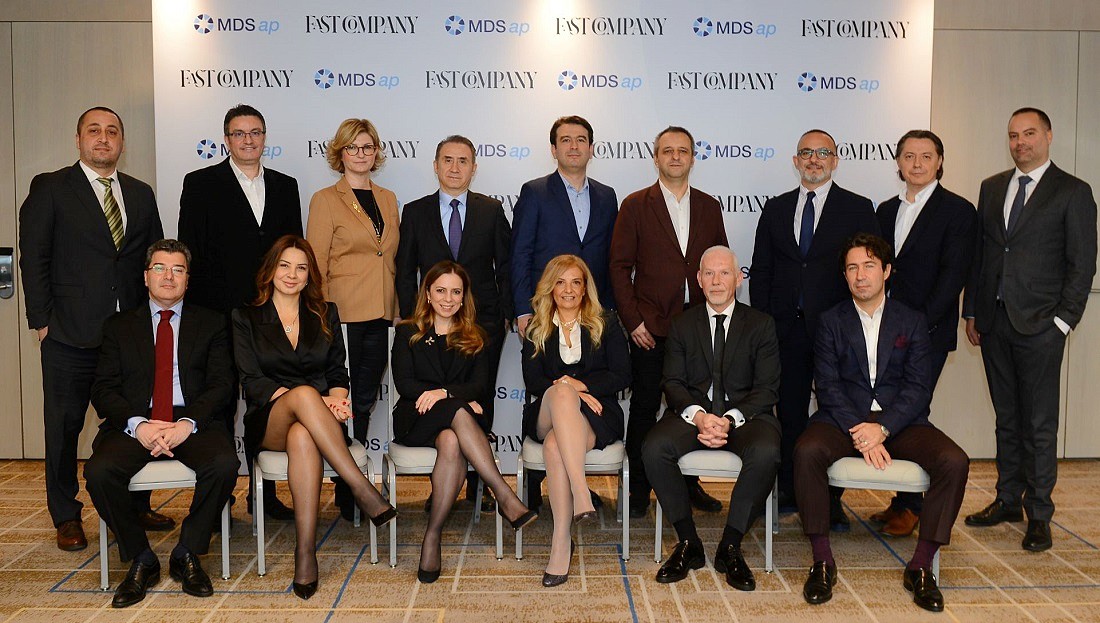 group photo of executives sitting in two rows against a logo covered background