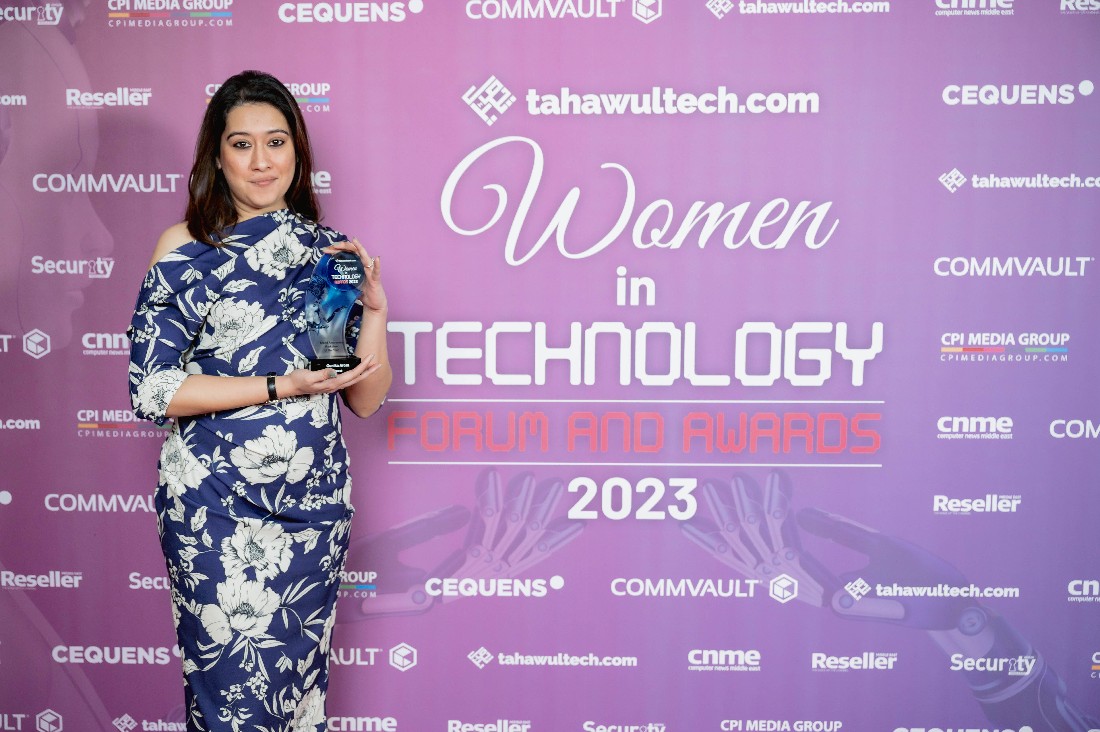 a woman in a blue dress with a white flowered pattern holds a trophy in front of a presentation background