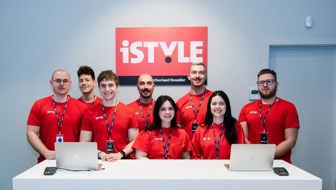 a group of colleagues who work together in a hi tech shop are seen in a photo. Many are wearing red t-shirts. 