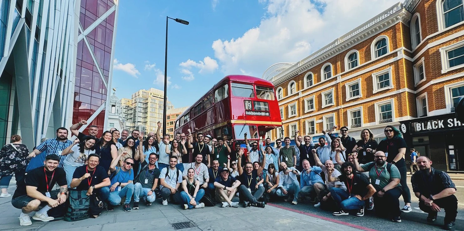 une grande photo de groupe prise à l’extérieur à Londres avec un bus rouge de Londres en arrière-plan. 