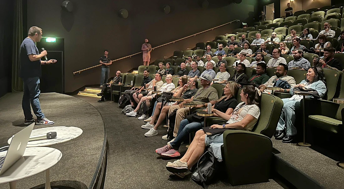  à gauche, un homme parle dans un micro et fait une présentation à un groupe de personnes dans un auditorium 