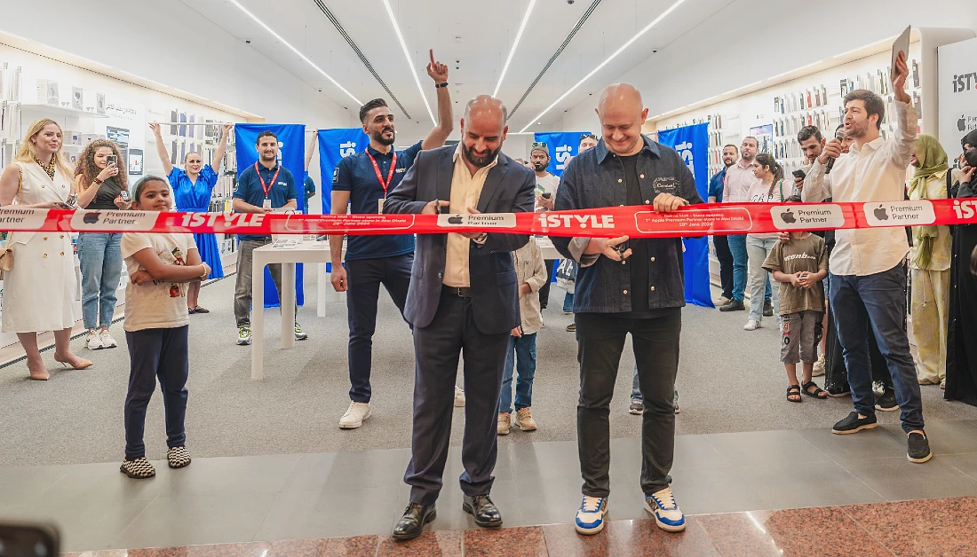 two men are seen cutting a red ribbon in front of a hi tech shop interior