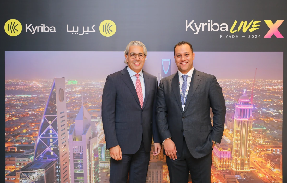 Two men in suits are seen in front of a display with the word kyriba seen prominently in English and Arabic