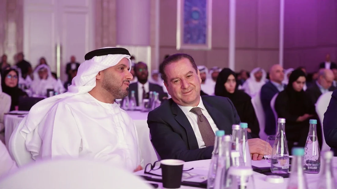 two men are seen smiling as they talk at a table at a hi tech summit