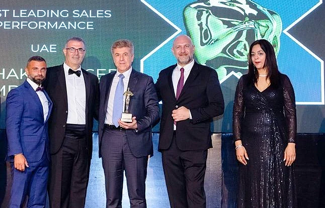 Five people are on a presentation stage with a man in the centre holding a trophy