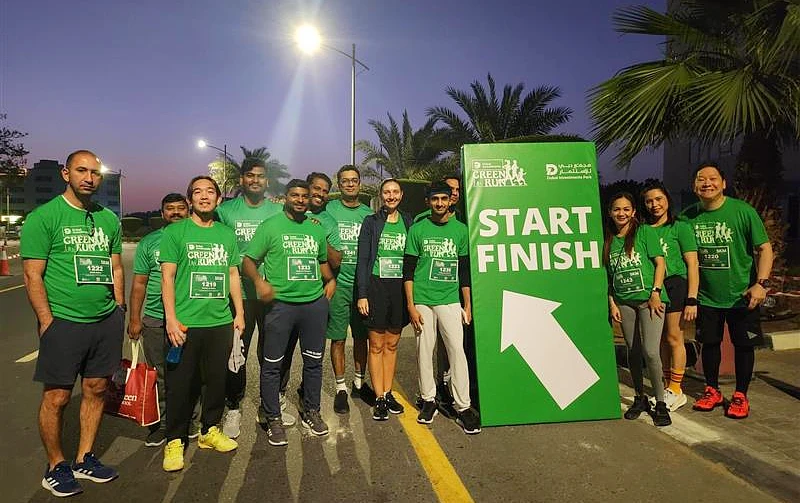 13 people in green t-shirts are gathered in a group photo after a run