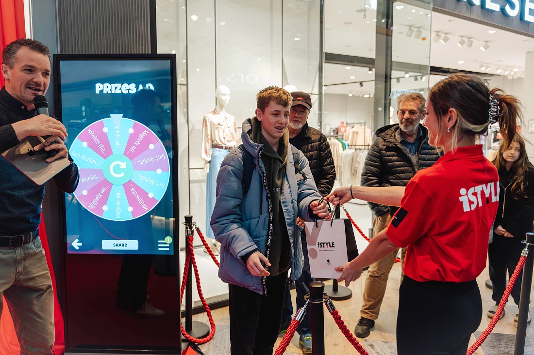 three people are seen at a busy hi tech shop with a prize being handed over to a customer