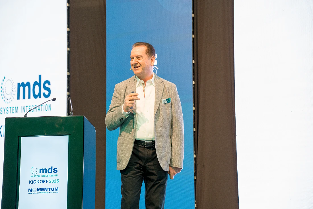 a man in a jacket speaks and smiles as he presents to an audience